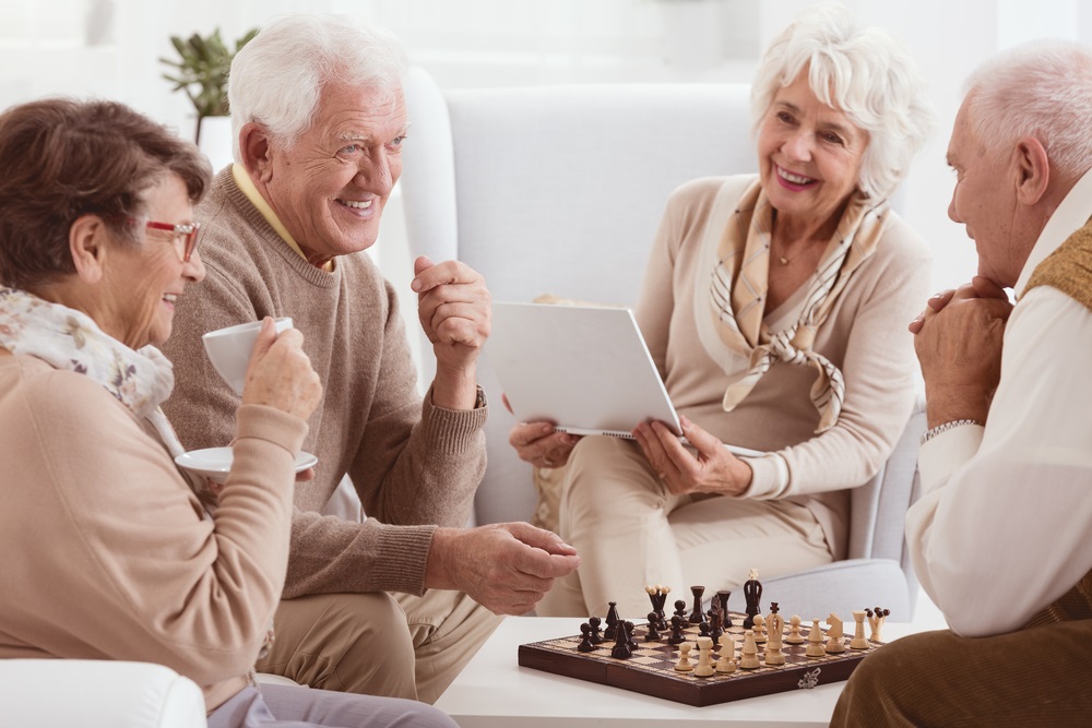 Four seniors playing with chess sharing the same smile small assisted living